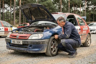 Mécanicien inspectant la suspension d'une Peugeot 106 Maxi de rallye amateur sur un parc assistance en gravier